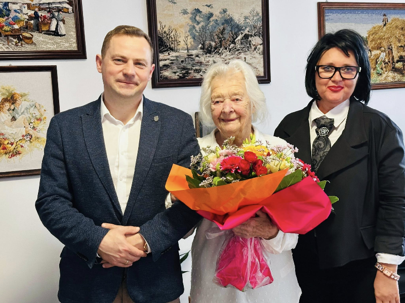 tzrzy osoby w środku stulatka trzymająca kwiaty 